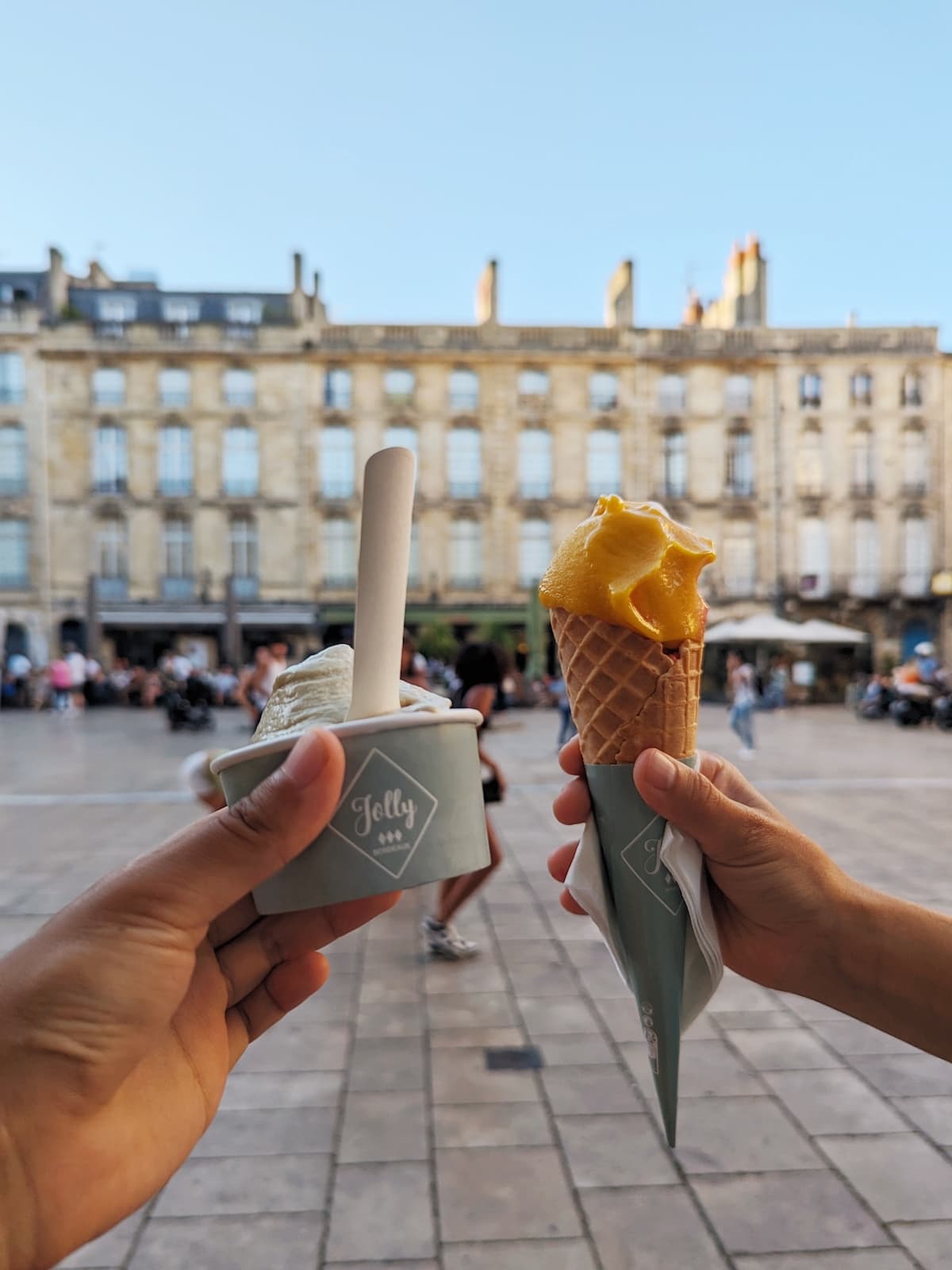 Ice cream in a cone and cup held up by two hands with the square in the background