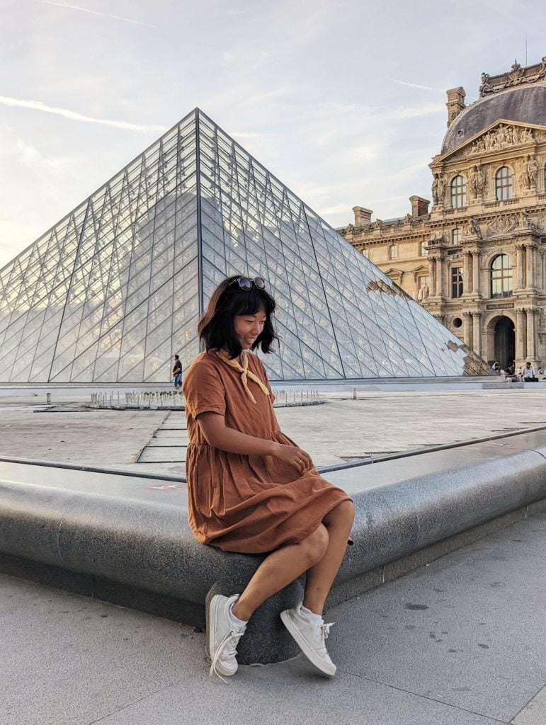 Me posting for a photo in front of the Louvre pyramids at the golden hour