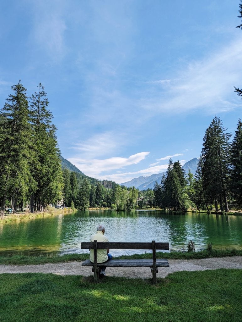 Lac des Gaillands on a clear day with an older man on the bench looking out at the river