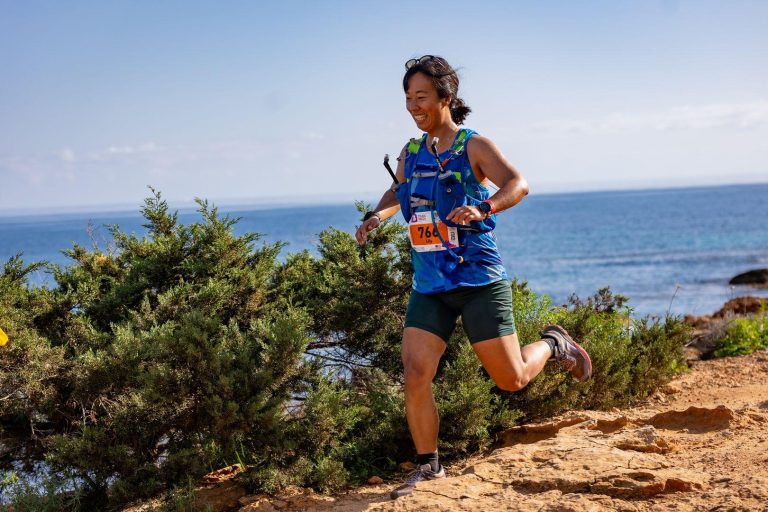 Me, an Asian woman, running downhill and smiling with the ocean in the background