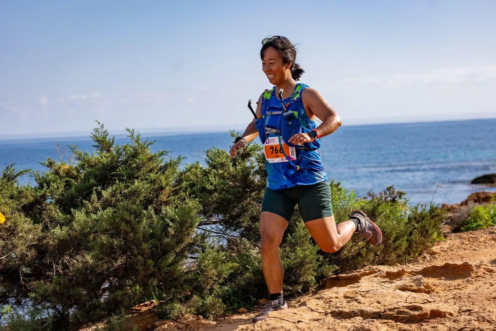 Me, an Asian woman, running downhill and smiling with the ocean in the background