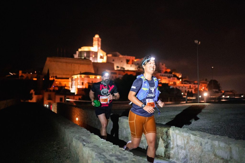 Me, an Asian woman, running with Ibiza Old Town in the background at night