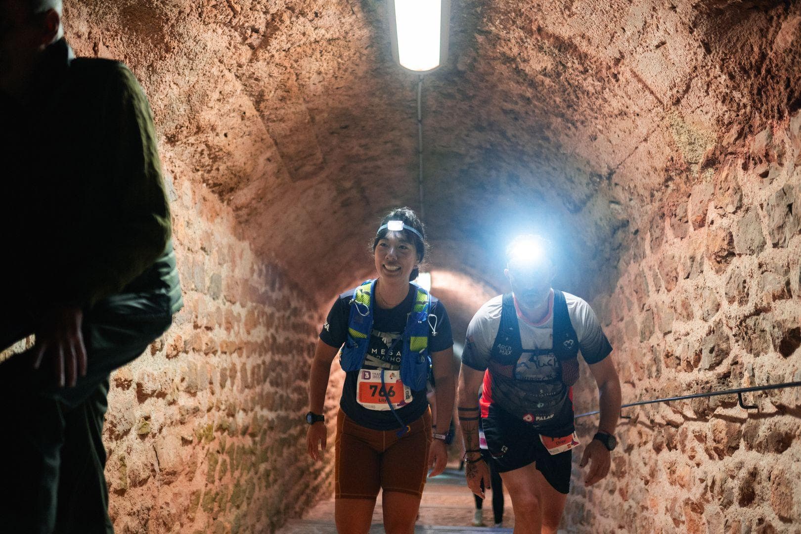 Me, an Asian woman, walking through a tunnel with a headlamp on during a race