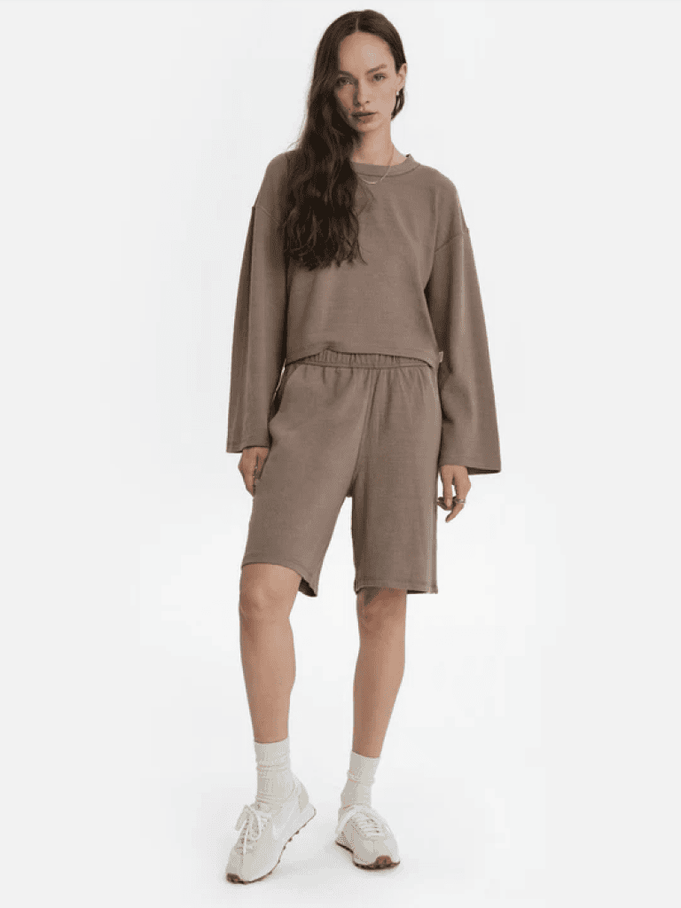 White woman with long brown hair wearing a gray tan set with long shorts