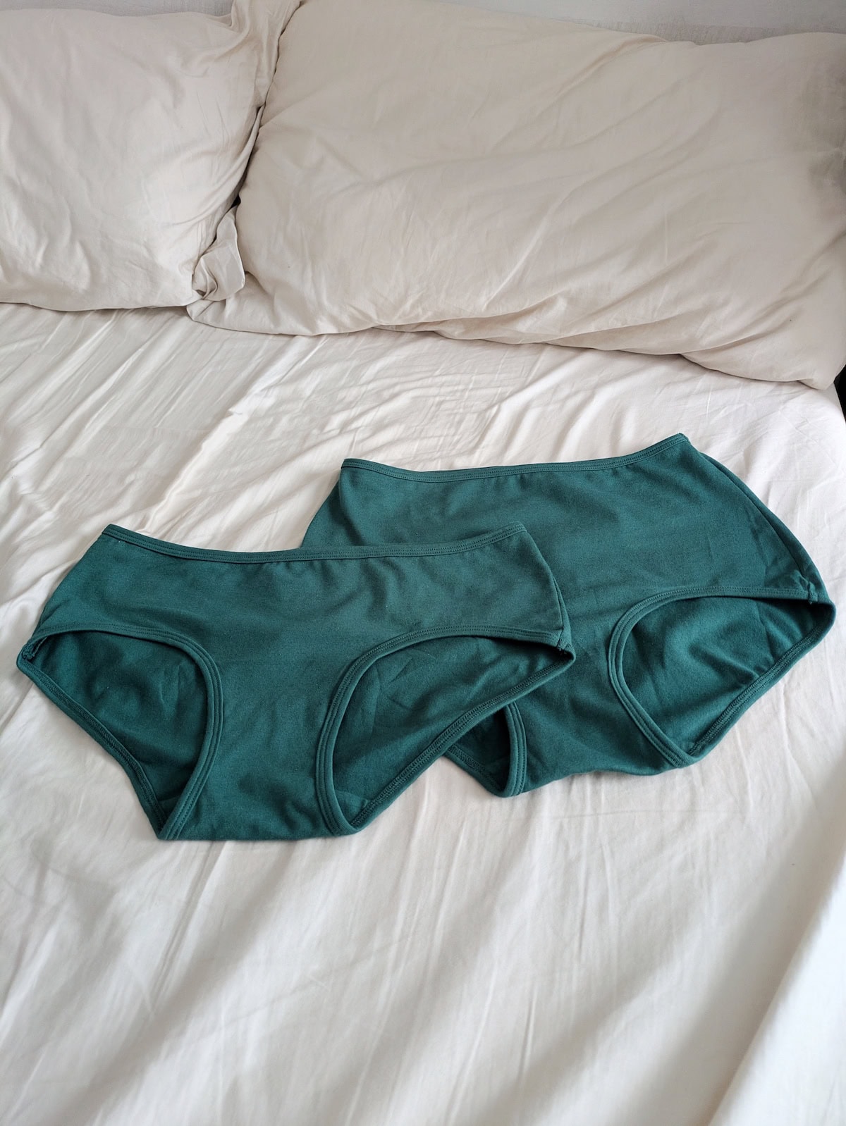 2 pairs of PROCLAIM underwear in lagoon (deep green) on a bed with white sheets