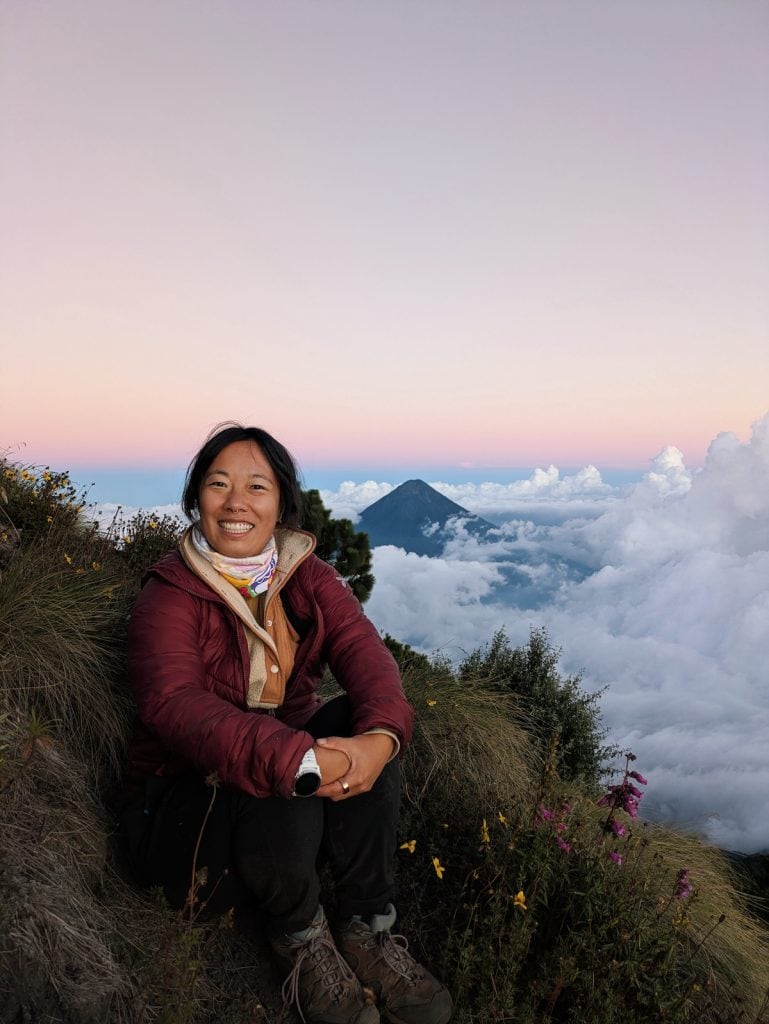 Me sitting in the grass at sunset with Agua Volcano in the background against a pink sky