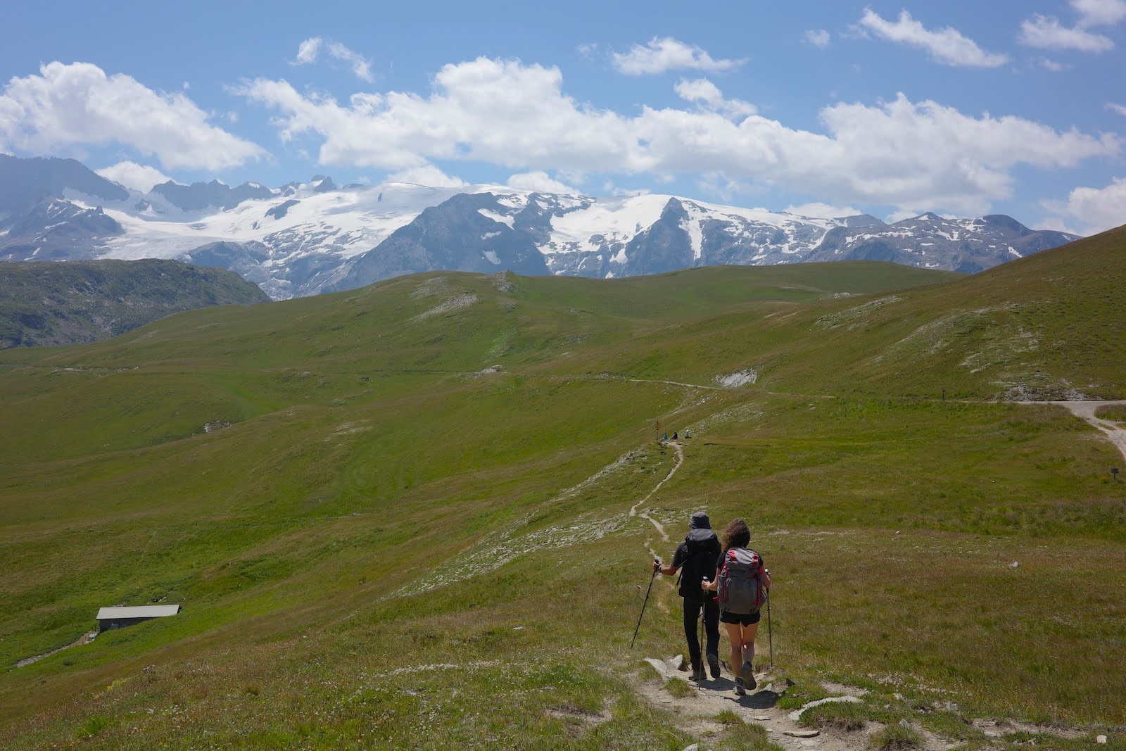 Photo of 2 people hiking on a grassy plain with snow-capped mountains in the background