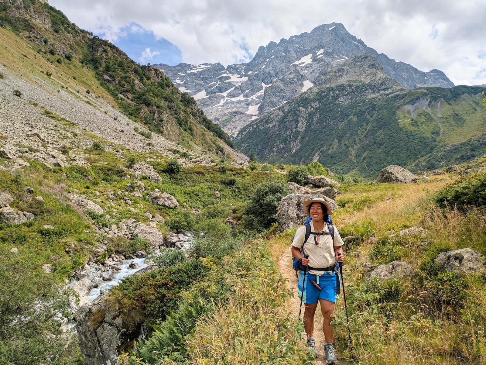 Me walking through a grassy trail with mountains in the background and a stream on the left
