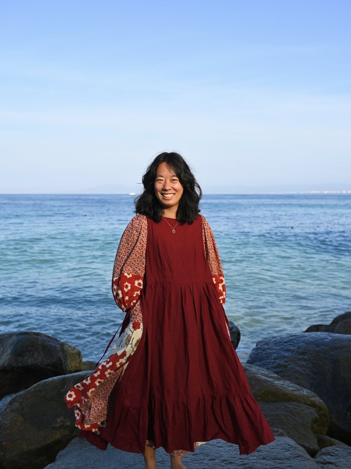 Me wearing the Son de Flor Ivy Dress in Burgundy Red over a patchwork dress by the ocean
