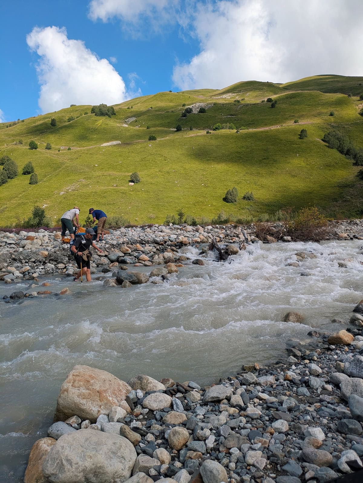 People crossing the white water river near Adishi Glacier