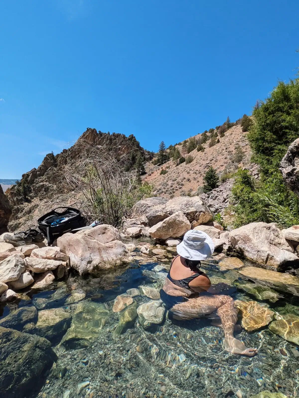 Me with a white sunhat on turning to look towards the mountains while soaking in Goldbug Hot Springs