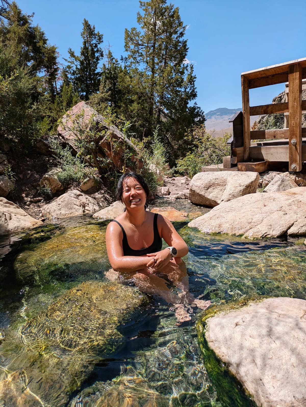 Me sitting in Goldbug Hot Springs with a footbridge behind me